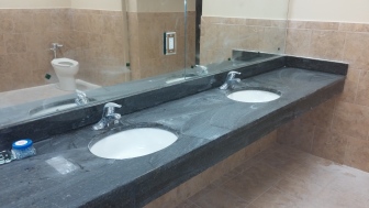 A bathroom inside the Maxx Fitness gym features black granite countertops and tile on its floors and walls.