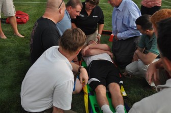 Saucon Valley athletic trainer Amy secures the head and neck of student volunteer Christian Carvis.